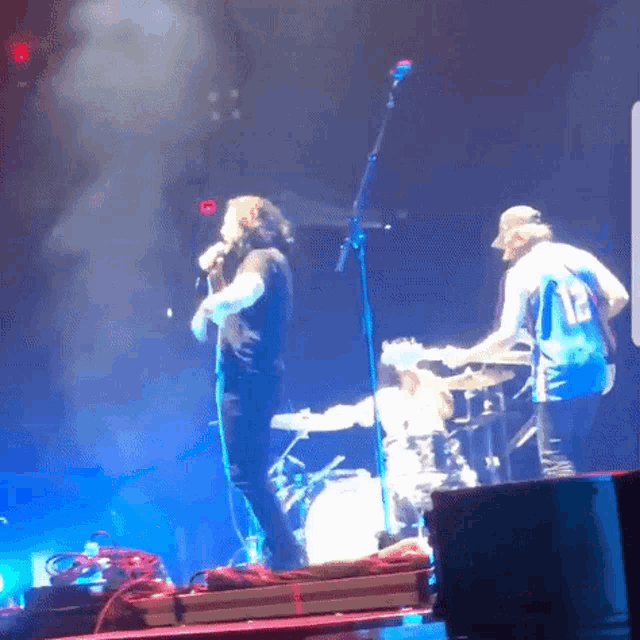 a man singing into a microphone while another man plays the drums