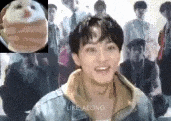 a man in a denim jacket is smiling in front of a group of people in a room .