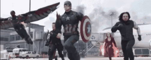 captain america is running with a shield in his hand while a group of people are running behind him .