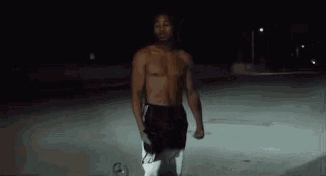a man without a shirt is standing on a skateboard at night .