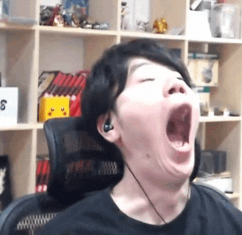 a man wearing headphones is yawning in front of a bookshelf .