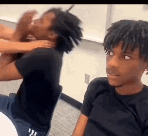 two young men are sitting next to each other in a classroom and one of them is holding another man 's head .