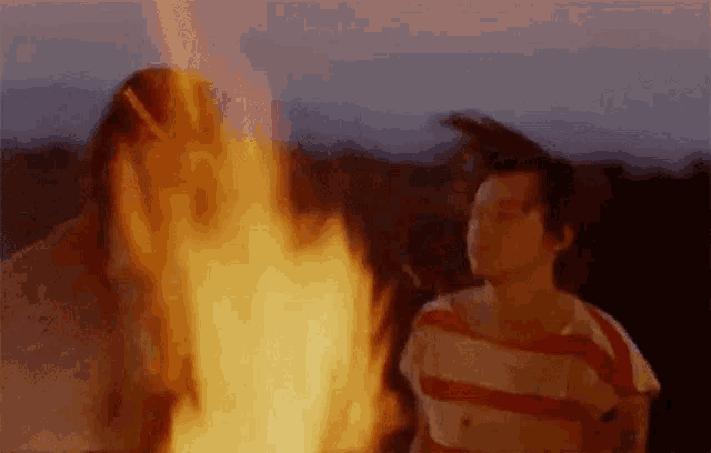 a man and a woman are standing next to a fire at night .