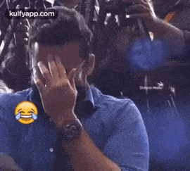 a man in a blue shirt is covering his face with his hand while a smiley face is behind him .