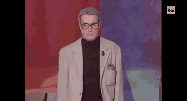 a man wearing glasses and a turtleneck is standing in front of a red background .