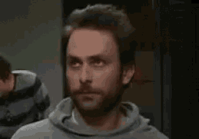 a man with a beard and a gray hoodie is looking at the camera .