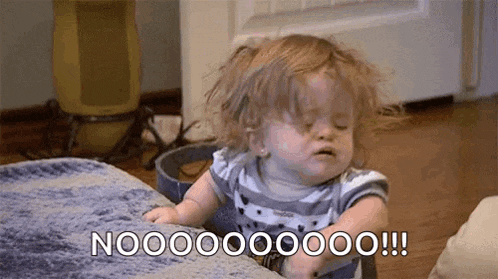 a baby girl is sitting on a couch with her eyes closed and making a face .
