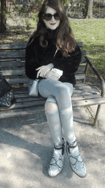 a woman is sitting on a park bench wearing sunglasses and snake print boots