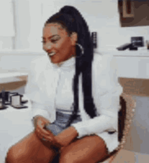 a woman is sitting on a chair with her legs crossed and smiling while holding a cell phone .