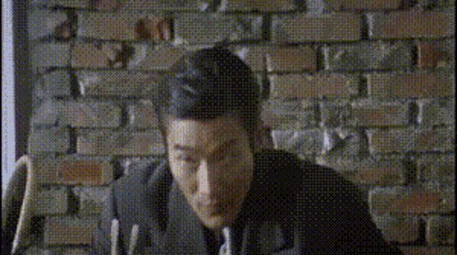 a man in a suit is sitting in front of a brick wall with chinese writing on it .