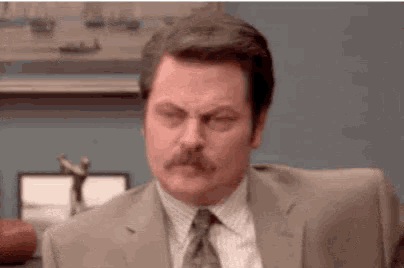 a man in a suit and tie with a mustache is sitting at a desk .