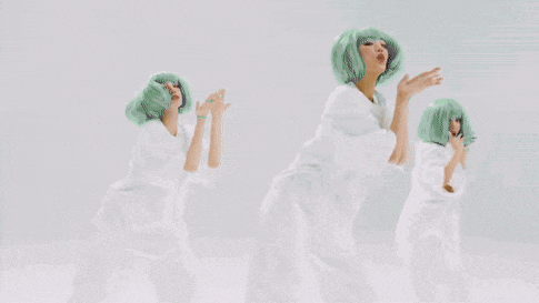 a woman with white hair is dancing with two other women in green overalls