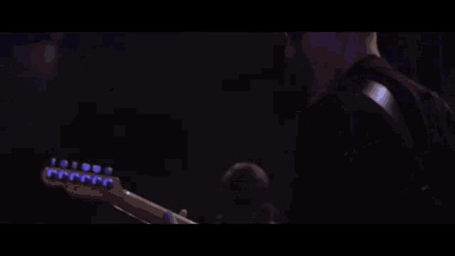 a man is playing a guitar on stage in a dark room .