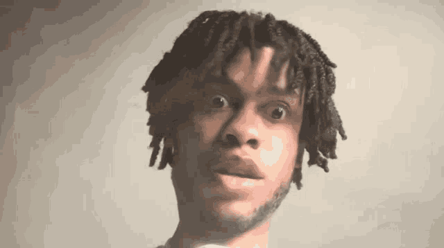 a young man with dreadlocks and a beard is making a funny face and looking at the camera .
