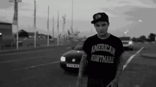 a man wearing an american nightmare t-shirt is standing in a parking lot