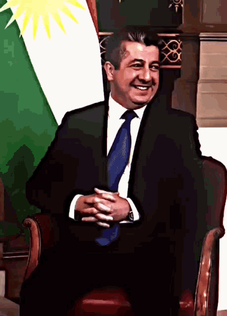 a man in a suit and tie sitting in front of a flag