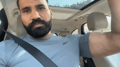 a man with a beard is sitting in a car with a seat belt on