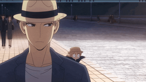 a man wearing a hat and a suit stands in front of a brick walkway