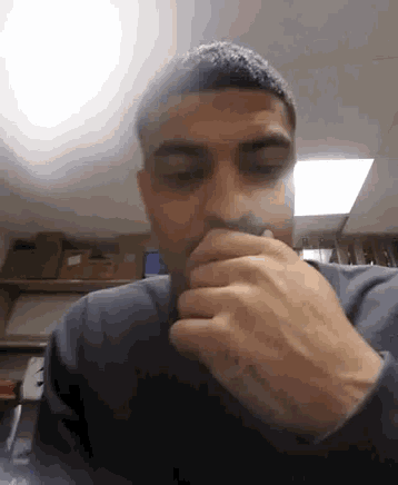 a man is covering his mouth with his hands in a dark room