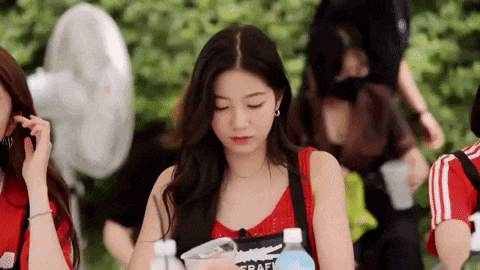 a woman in a red tank top is holding a bottle of water and talking on a cell phone .