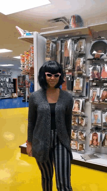 a woman wearing a wig and pink sunglasses stands in front of a display of costumes in a store