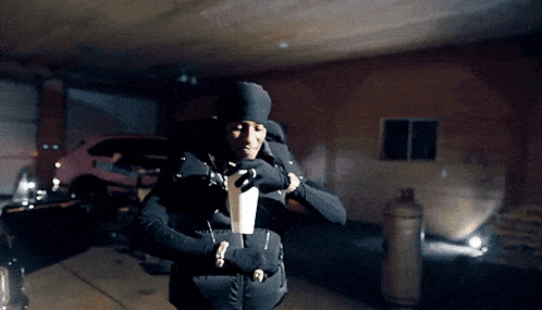 a man in a black jacket and hat is standing in a garage