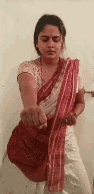 a woman in a red and white sari is standing in front of a door .