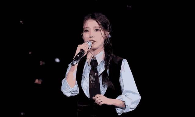 a woman is singing into a microphone while wearing a blue shirt and tie .