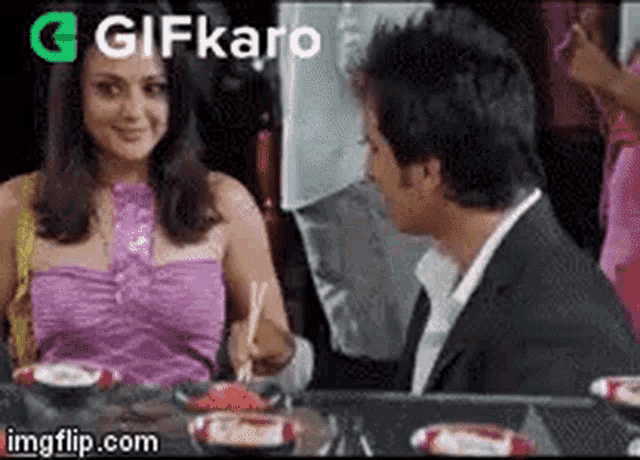 a man and a woman are sitting at a table and eating food .