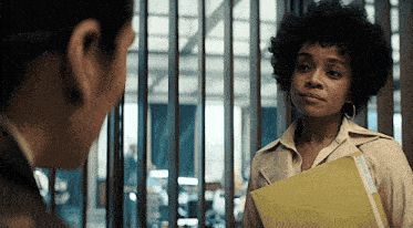 a woman in a trench coat is holding a folder and talking to another woman
