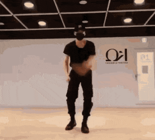 a man wearing a mask is dancing in a room with a greek letter on the wall .