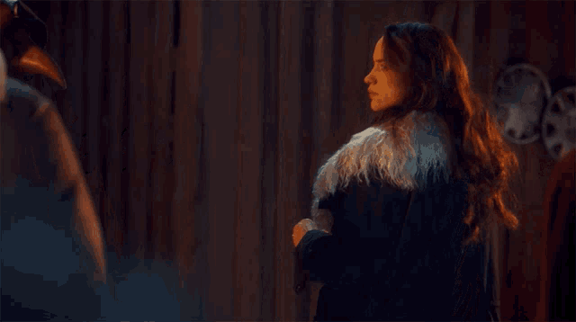 a woman in a fur coat stands in front of a wall with the words good to know above her