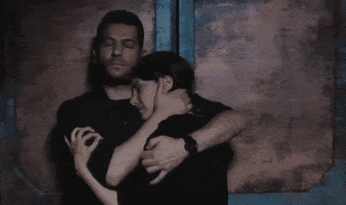 a man and a woman hugging each other in front of a wall