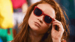 a woman with red hair is wearing sunglasses and looking at the camera .