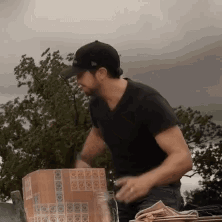 a man in a black shirt and hat is standing next to a cardboard box .