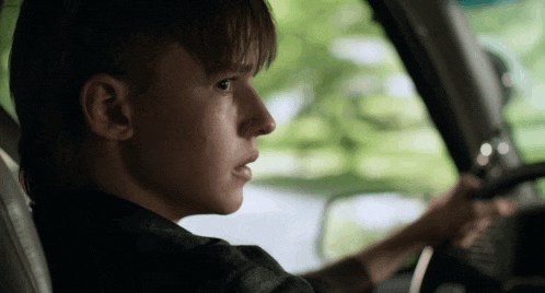 a young man is driving a car and looking out the window