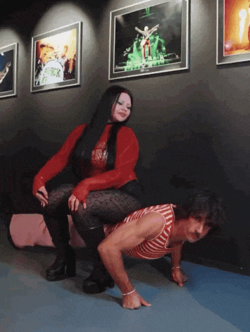 a woman is sitting on a man 's shoulders in front of a wall with a picture of a band called freak