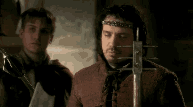 a man with a crown on his head is standing next to another man holding a sword and making a face .