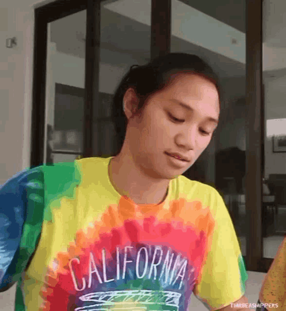 a woman wearing a california tie dye shirt looks down