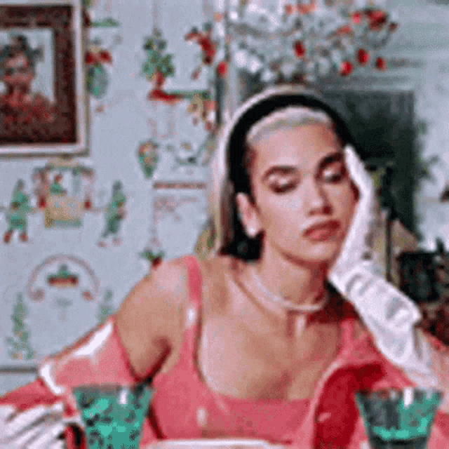 a woman in a pink dress and white gloves is sitting at a table with glasses of water .