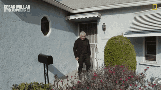 a man is standing in front of a blue house with the words cesar millan better human better dog