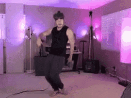 a man in a black tank top is dancing in a room with purple lights .