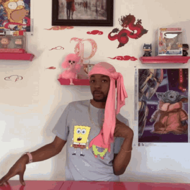 a man wearing a spongebob shirt is standing in front of a shelf with a picture of the baby yoda on it