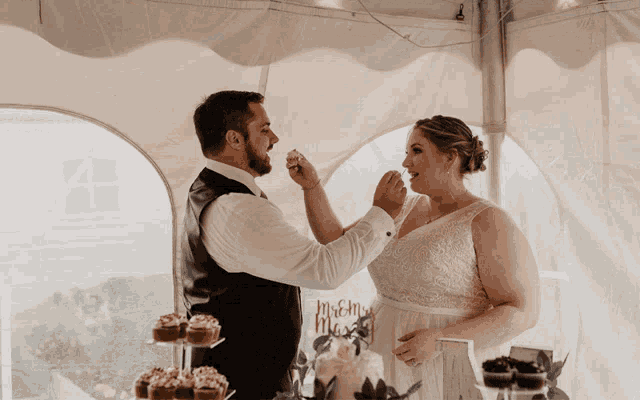 a bride and groom are cutting their wedding cake under a tent with cupcakes on display