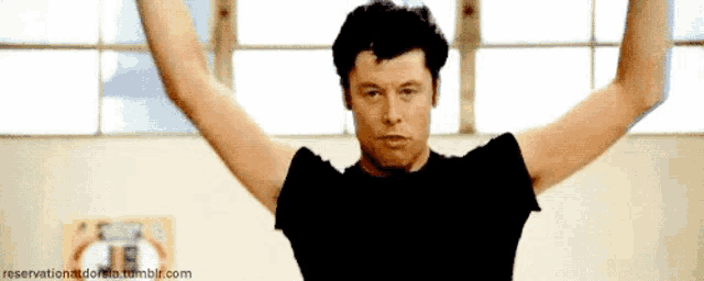 a man in a black shirt has his arms outstretched in a gym