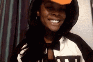 a woman wearing a hoodie and a baseball cap is smiling .