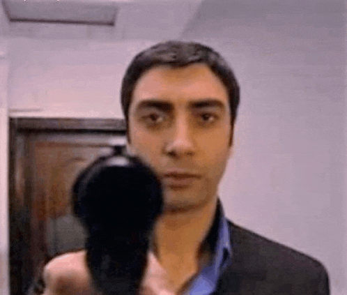 a man in a suit is holding a gun in front of his face and pointing it at the camera .