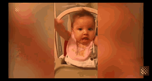 a baby is sitting in a high chair wearing a bib and making a funny face .