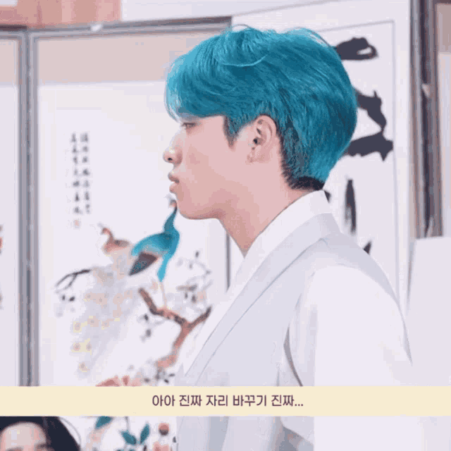 a man with blue hair stands in front of a painting with chinese writing on it