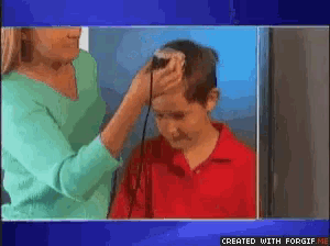 a woman is cutting a young boy 's head with a razor